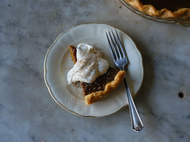 a spice of pumpkin pie on a plate with a golden crust and dollop of whipped cream