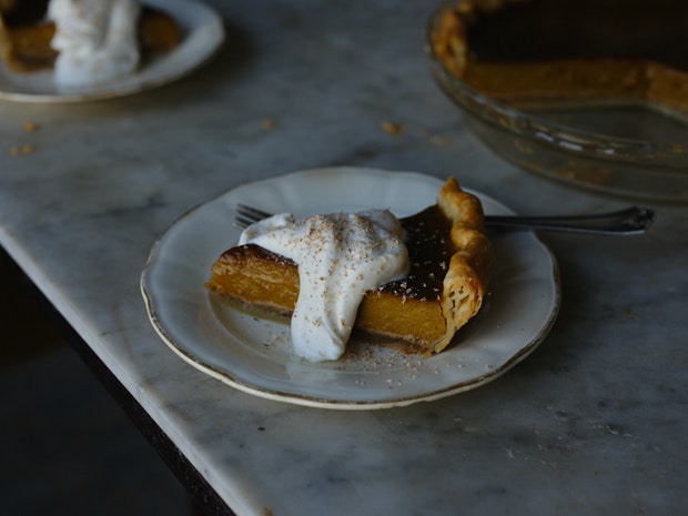 a spice of pumpkin pie on a plate with a golden crust and dollop of whipped cream